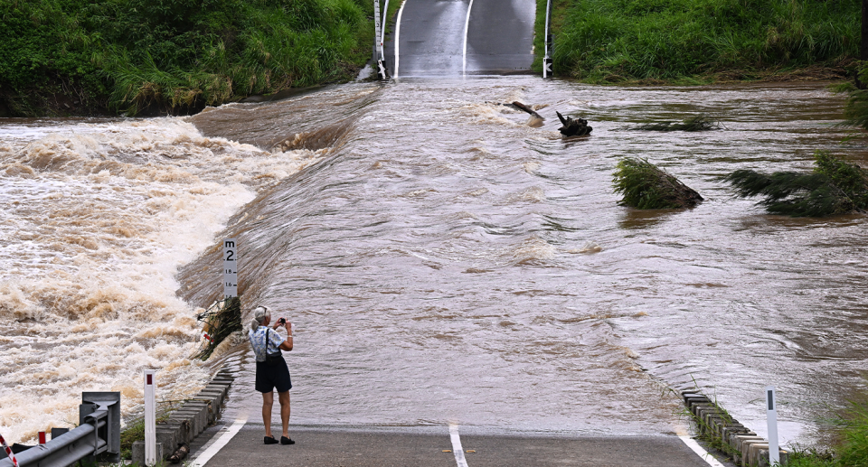A woman stands by a body of water flowing over a cut off road on Coomera River on Gold Coast on January 2. 