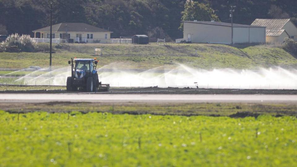 A tractor tills a field as irrigation sprinklers spray near Highway 1 and Halcyon Road in Arroyo Grande on Dec. 4, 2023.