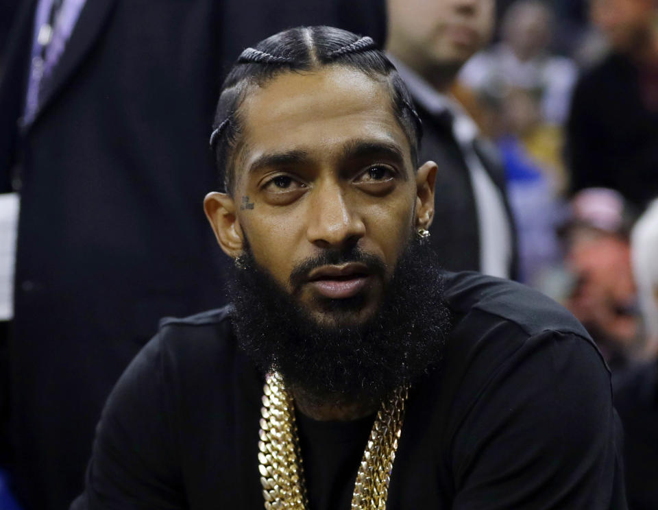 Rapper Nipsey Hussle watches an NBA basketball game between the Golden State Warriors and the Milwaukee Bucks in Oakland, Calif. on March 29, 2018. The widely respected West Coast rapper was shot and killed outside his Los Angeles clothing store on March 31. He was 33. (AP Photo/Marcio Jose Sanchez)