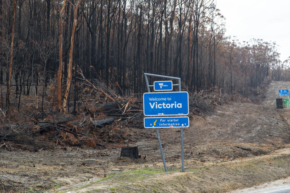 A Welcome to Victoria sign with burnt forest behind it.