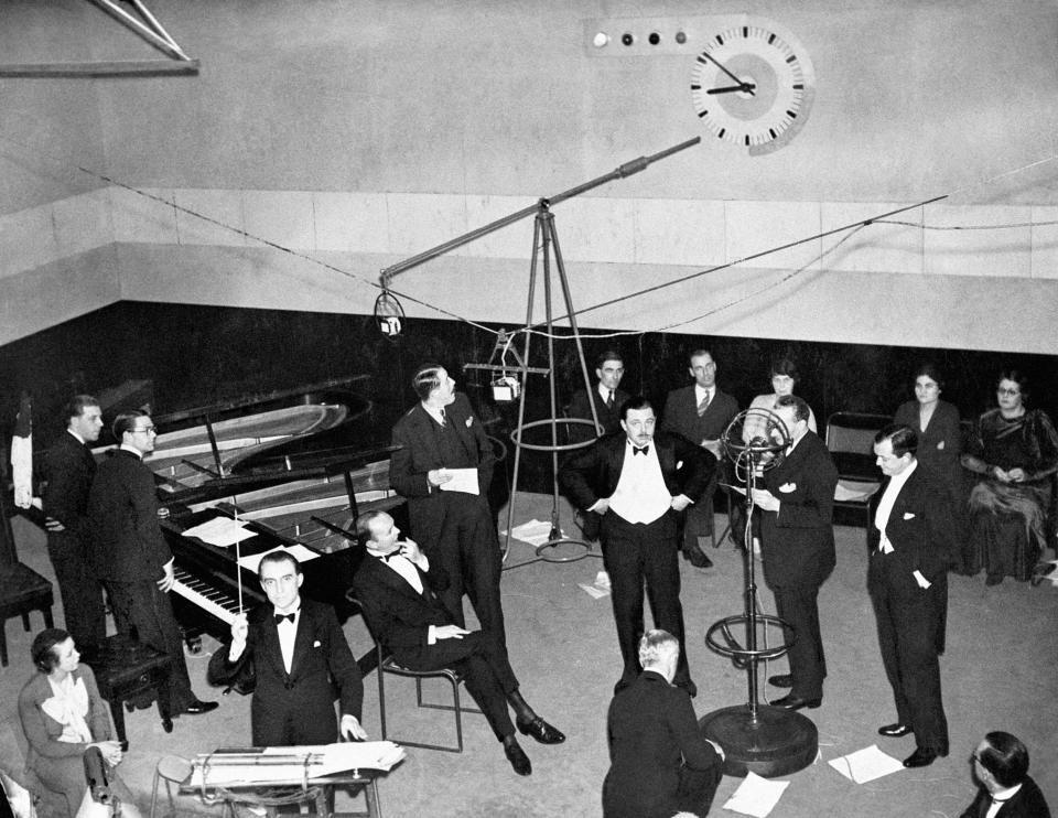A scene in a 1930s BBC recording studio showing Christopher Stone, wearing a dinner jacket, bidding listeners 'Good Evening'. Stone is considered to be the first disc jockey in the UK.