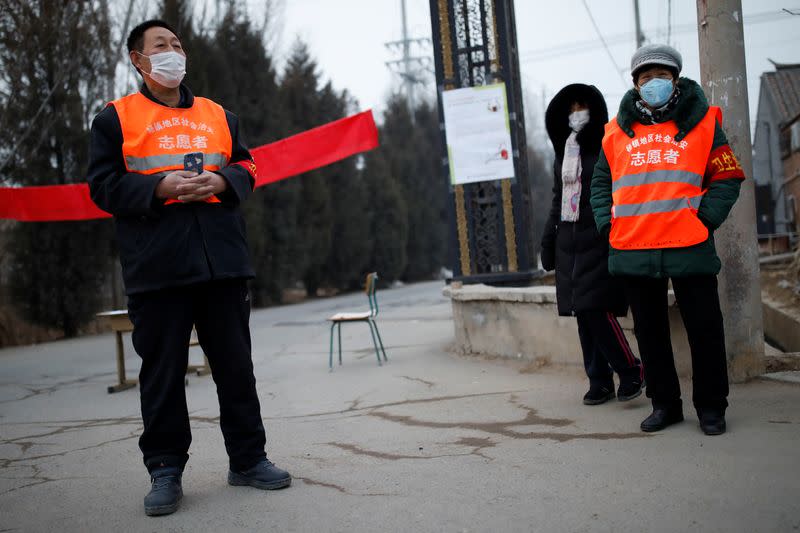 Village committee members wearing face masks and vests stand at the entrance of a community to prevent outsiders from entering, as the country is hit by an outbreak of the new coronavirus, in Tianjiaying village, outskirts of Beijing