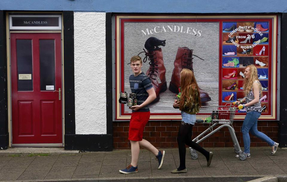 Youths walk past a shop, which has been covered with artwork to make it look more appealing, in the village of Bushmills on the Causeway Coast August 20, 2013. One of the homes of Irish whiskey has taken a scheme developed in Northern Ireland of erecting fake shop fronts where derelict buildings lie and has truly run with it in a bid to woo tourists. Bushmills, best known as the village where the whiskey of the same name was distilled for the first time 400 years ago, is now also becoming recognisable for the artwork and graphics that brighten up shop fronts left empty during the economic downturn. Picture taken August 20, 2013. REUTERS/Cathal McNaughton (NORTHERN IRELAND - Tags: BUSINESS SOCIETY TRAVEL) ATTENTION EDITORS: PICTURE 18 OF 20 FOR PACKAGE 'NORTHERN IRELAND'S TROMPE L'OEIL' SEARCH 'BUSHMILLS ART' FOR ALL IMAGES