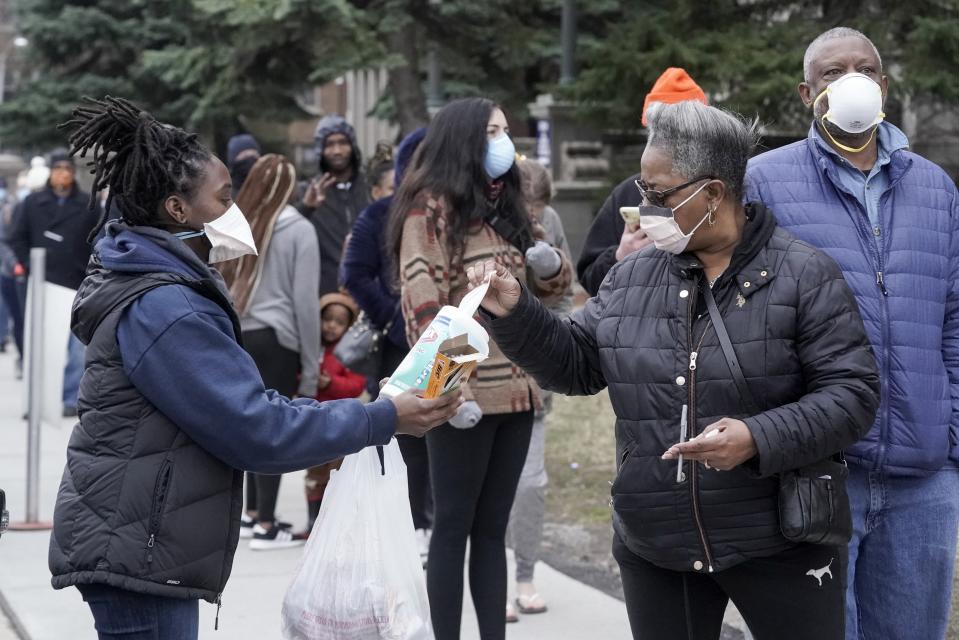 A worker hands out disinfectant wipes and pens as voters line up outside Riverside High School for Wisconsin's primary election Tuesday April 7, 2020, in Milwaukee. The new coronavirus causes mild or moderate symptoms for most people, but for some, especially older adults and people with existing health problems, it can cause more severe illness or death. (AP Photo/Morry Gash)