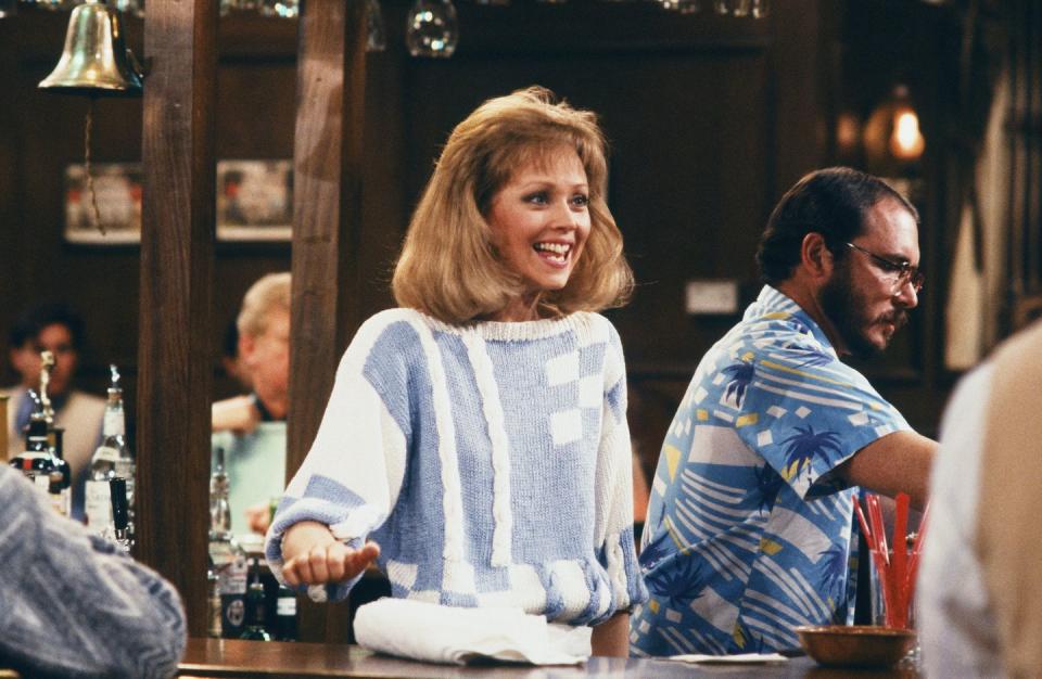 cheers diane chambers, played by shelley long, standing behind the bar and smiling