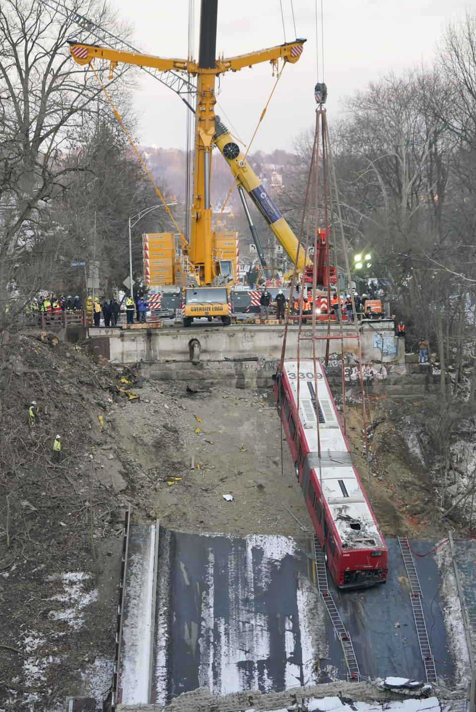 Cranes lift the bus that was on a bridge when it collapsed Friday during the recovery process on Monday Jan. 31, 2022 in Pittsburgh's East End. (AP Photo/Gene J. Puskar)