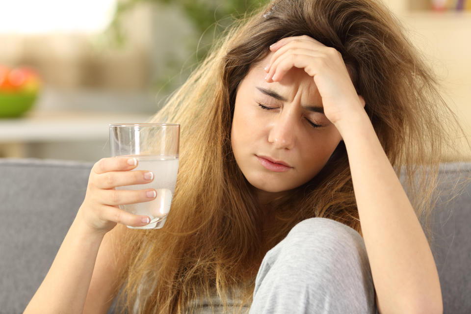 Front view of a teen with tousled hair suffering head ache sitting on a couch in the living room at home