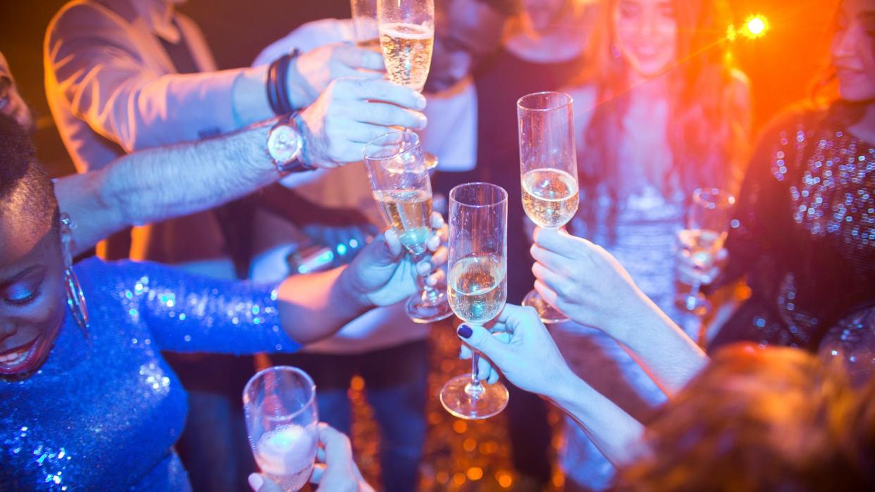 High angle view at multi-ethnic group of laughing young people enjoying dance party in nightclub and drinking champagne, focus on clinking glasses.