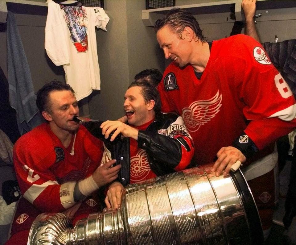 FILE - In this June 16, 1998 file photo, Vladimir Konstantinov, center, holds the Stanley Cup in his lap and pours champagne for defenseman Viacheslav Fetisov, left, as center Igor Larionov looks on in a post game locker room celebration after beating the Washington Capitals 4-1 in Game 4 to take the Stanley Cup at the MCI Center in Washington. More than two decades since Fetisov and the “Russian Five” shattered the myth that NHL teams couldn’t win with players from a nation unpopular in North America, the St. Louis Blues’ Russian Two of Vladimir Tarasenko and Ivan Barbashev are one victory away from lifting the same Cup after being inspired by the generation of countrymen who endured so much to get there. (AP Photo/Wilfredo Lee, File)