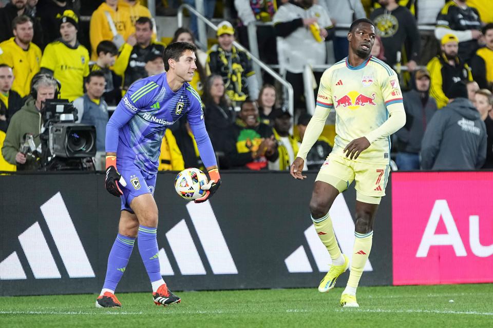 Mar 16, 2024; Columbus, Ohio, USA; Columbus Crew goalkeeper Patrick Schulte (28) smiles as he picks up the ball in front of New York Red Bulls forward Cory Burke (7) during the second half of the MLS soccer match at Lower.com Field. Mandatory Credit: Adam Cairns-USA TODAY Sports