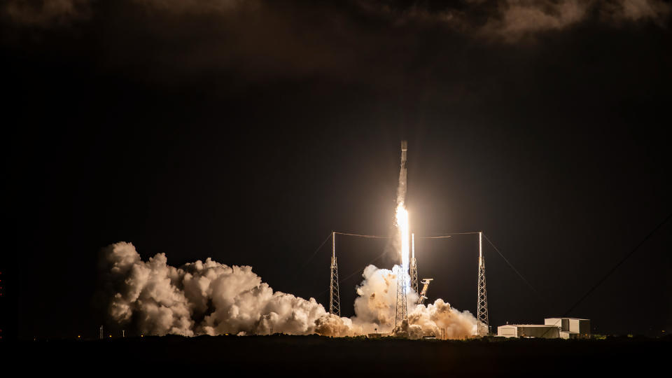 a black-and-white spacex falcon 9 rocket rises off a launch pad at night.