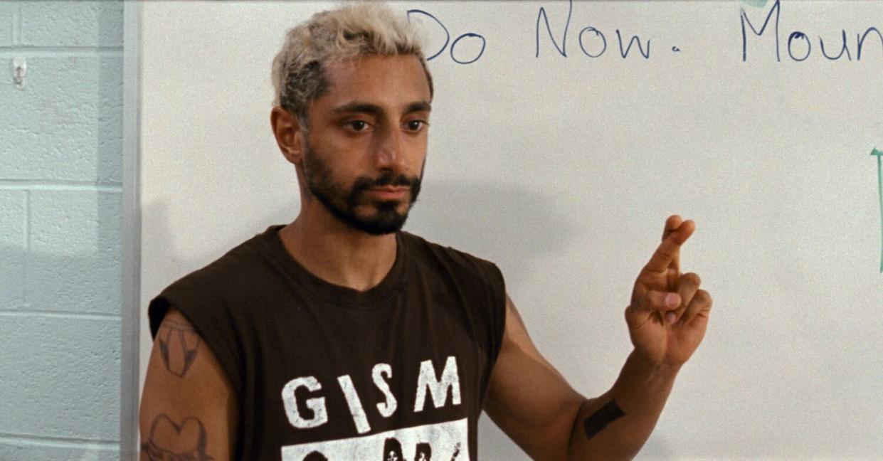 A man in a sleeveless band T-shirt holds up a hand with his fingers crossed.