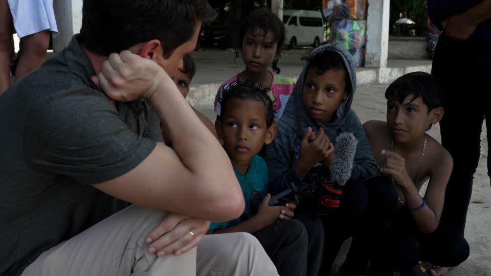 Joandry, 6, center holds the microphone while his sister Sofia, 12, and cousin Mathias, 9, talk to CNN's David Culver in Ciudad Hidalgo, Mexico, on the banks of the Suchiate River. - David von Blohn/CNN