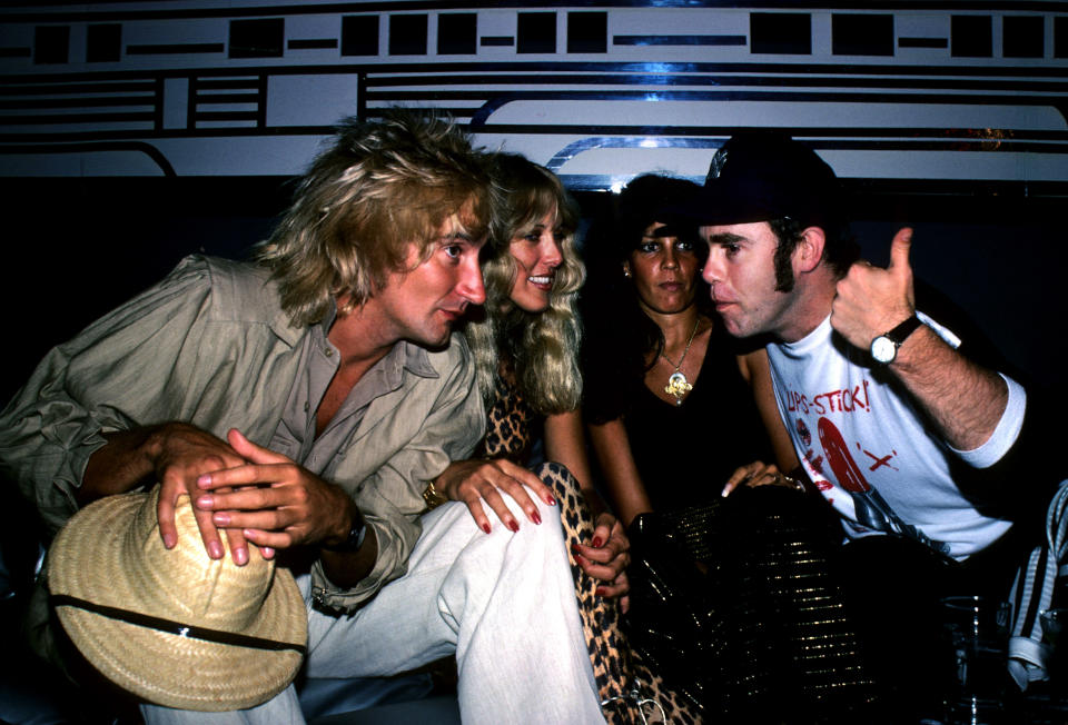 British pop singer Elton John (right), Lana Hamilton (second left), wife of actor George Hamilton, and rock singer Rod Stewart (left) at New York's Studio 54, to celebrate at a party given by RCA Records, who signed John to a contract with the recording company.