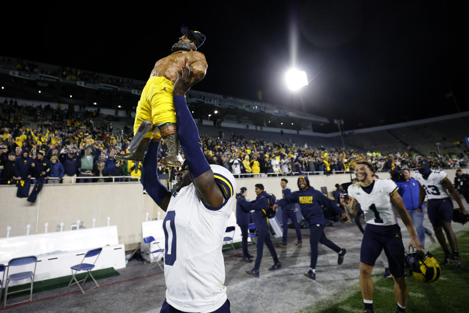 Michigan's Mike Sainristil, front left, carries the Paul Bunyan trophy after defeating Michigan State in an NCAA college football game, Saturday, Oct. 21, 2023, in East Lansing, Mich. (AP Photo/Al Goldis)