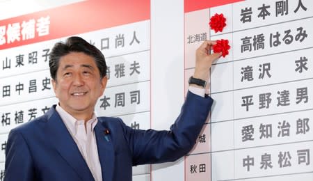 Japan's Prime Minister Shinzo Abe, who is also leader of the ruling Liberal Democratic Party (LDP), puts a rosette on the name of a candidate who is expected to win the upper house election, at the LDP headquarters in Tokyo