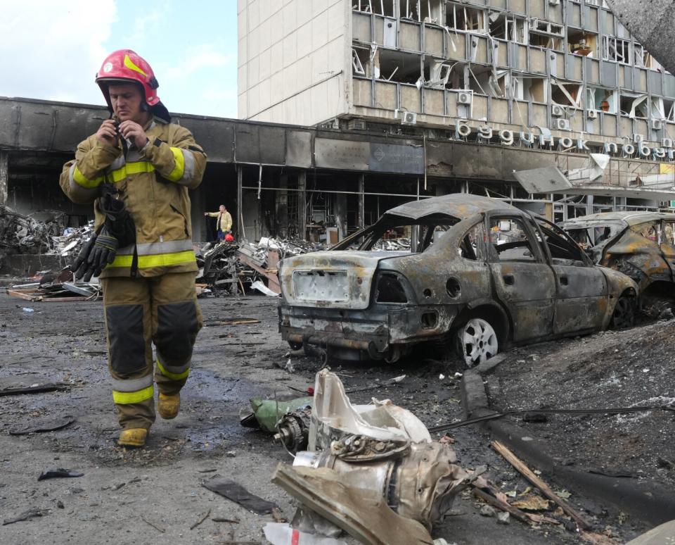 A firefighter stands near burned cars and a building with its windows blown out