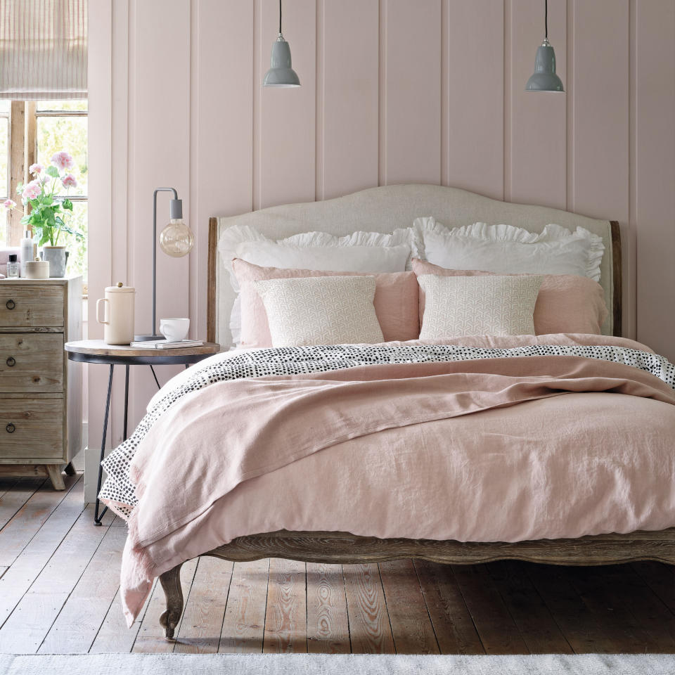 Pink panelled bedroom wall with bed with light pink bedding, bedside table, dresser