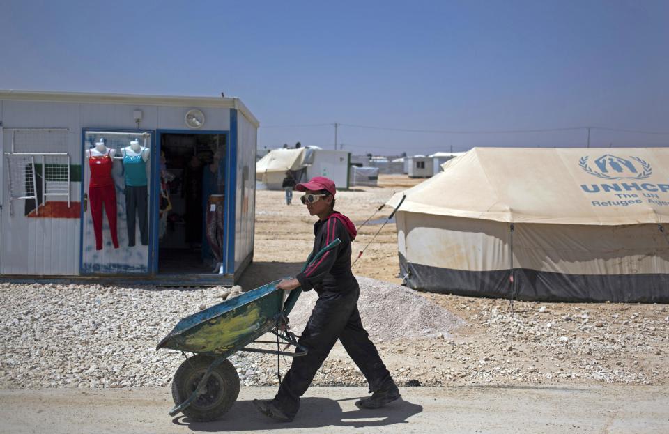 In this Thursday April 17, 2014 photo, a Syrian boy wearing sunglasses passes by a caravan used as a clothing shop at Zaatari refugee camp, near the Syrian border in Jordan. Some residents, frustrated with Zaatari, the region's largest camp for Syrian refugees, set up new, informal camps on open lands, to escape tensions and get closer to possible job opportunities.(AP Photo/Khalil Hamra)