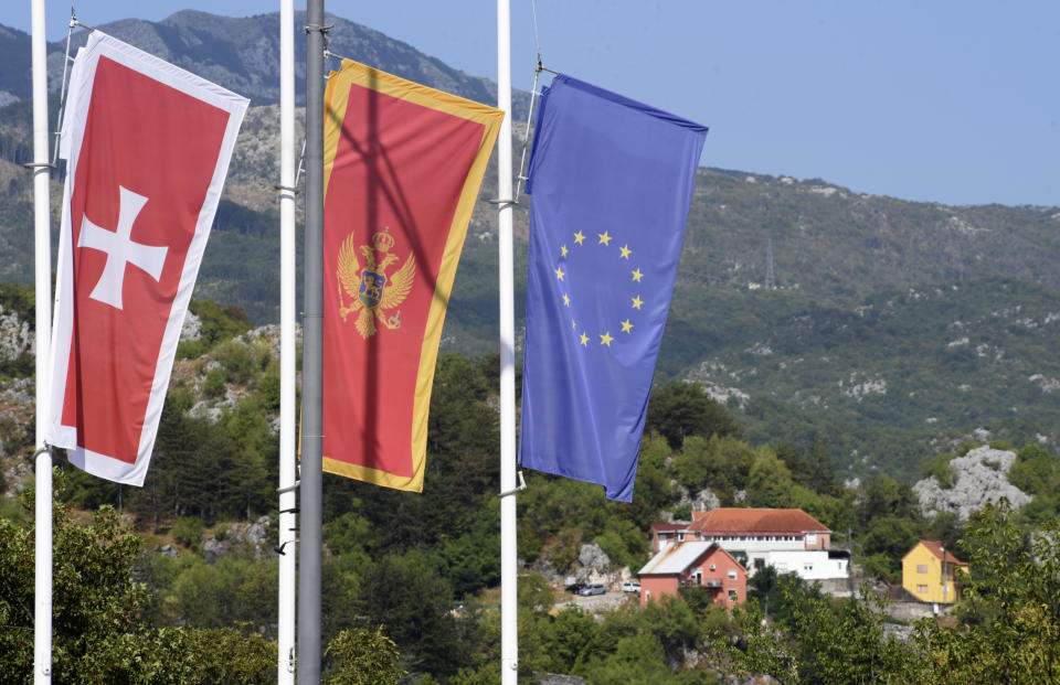 Banderas ondean a media asta frente al sitio de una masacre en Cetiña, 30 kilómetros al oeste de Podgorica, Montenegro, sábado 13 de agosto de 2022. En la víspera, un hombre empezó a disparar en la calle y mató a varias personas antes de que lo abatiera un transeúnte. (AP Foto/Risto Bozovic)