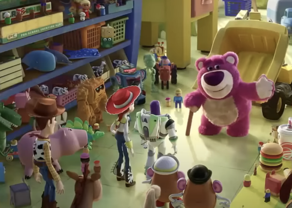 Woody, Buzz Lightyear, and other toys look at a waving Lotso in a toy room