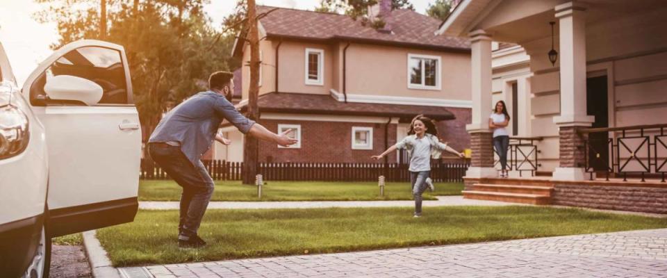 Happy family. Dad came home, daughter is running to meet him while wife is waiting on the house's porch.