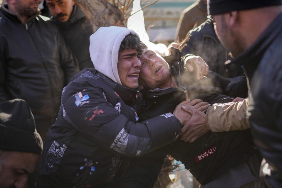 A young man in the center cries out while being hugged by another man. Steam is rising from their faces in cold weather