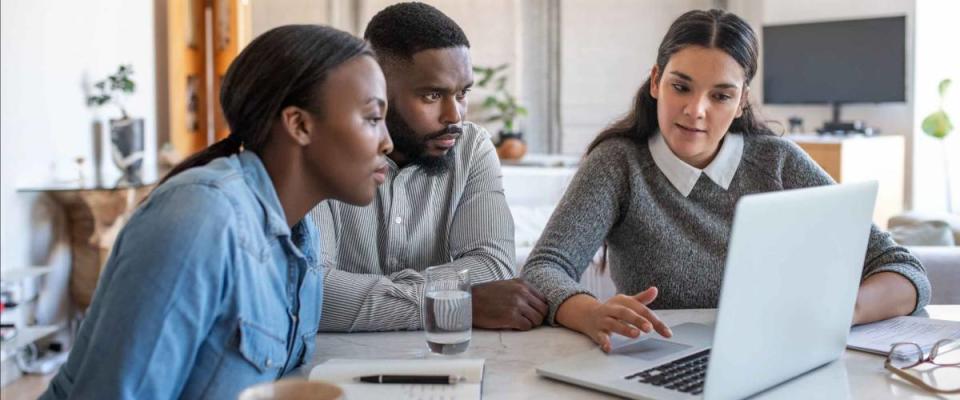 Financial planner going over savings plans on a laptop with a young African American couple at a table in their living room at home