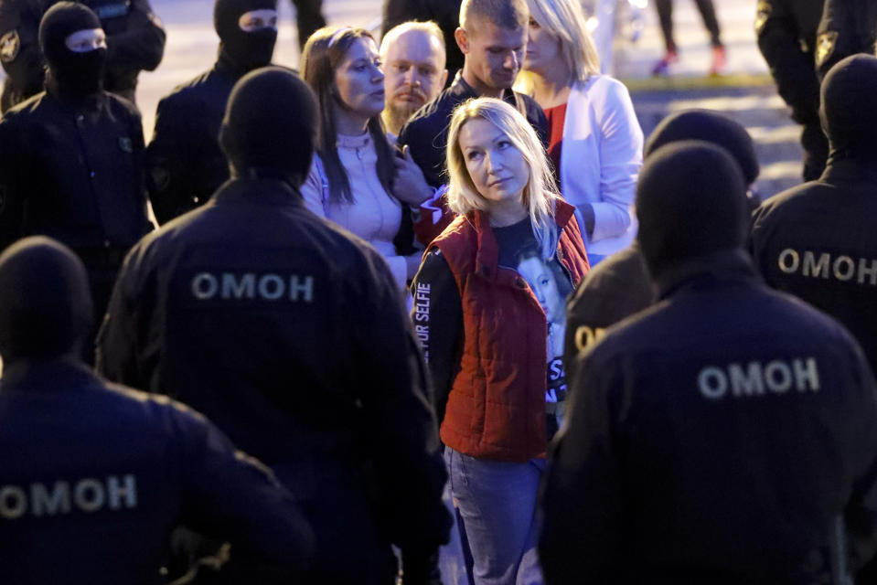 A woman looks at police surround protesters during a Belarusian opposition supporters rally at Independence Square in Minsk, Belarus, Wednesday, Aug. 26, 2020. Protests demanding the resignation of Belarus' authoritarian President Alexander Lukashenko have entered their 18th straight day on Wednesday. (AP Photo/Dmitri Lovetsky)