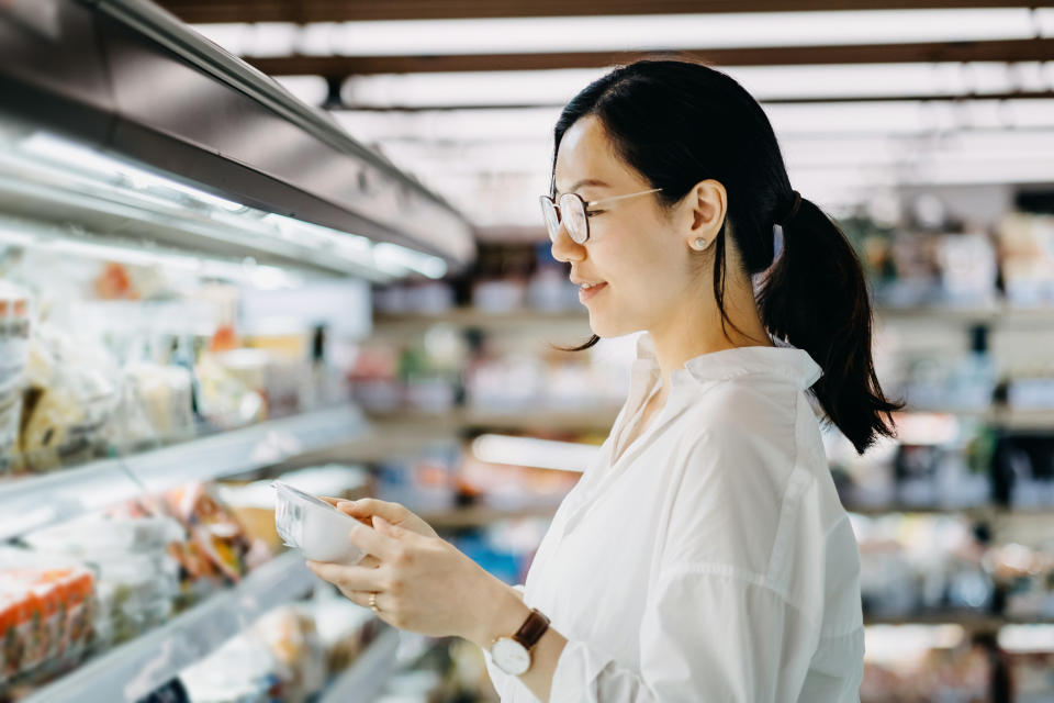 Young Asian woman grocery shopping in supermarket and reading nutrition label on a packet of fresh egg