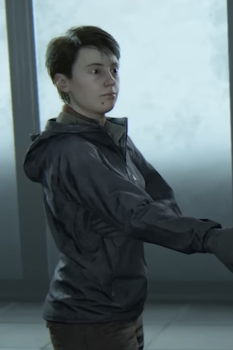 Mel in The Last of Us Part II standing indoors, facing sideways, wearing a leather jacket