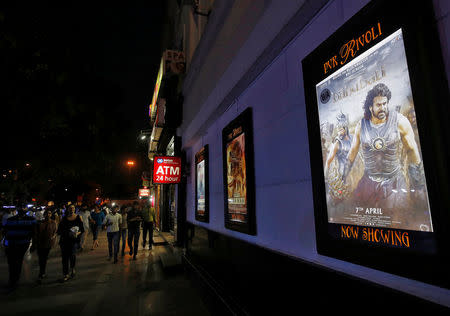 People walk past a poster of an Indian movie "Baahubali: The Beginning" outside a movie theater in New Delhi, India, April 12, 2017. REUTERS/Adnan Abidi