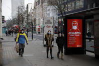 People wearing face masks to curb the spread of coronavirus walks past a social distancing sign on Oxford Street in London, Friday, Jan. 15, 2021, during England's third national lockdown since the coronavirus outbreak began. The U.K. is under an indefinite national lockdown to curb the spread of the new variant, with nonessential shops, gyms and hairdressers closed, most people working from home and schools largely offering remote learning. (AP Photo/Matt Dunham)