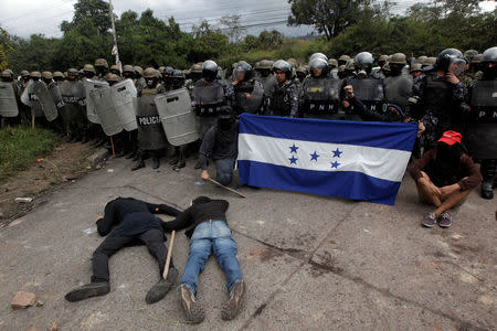 Opposition supporters hold a Honduran flag as others lie on the floor in front of security forces during a protest over a contested presidential election with allegations of electoral fraud in Tegucigalpa, Honduras, December 22, 2017. REUTERS/Jorge Cabrera