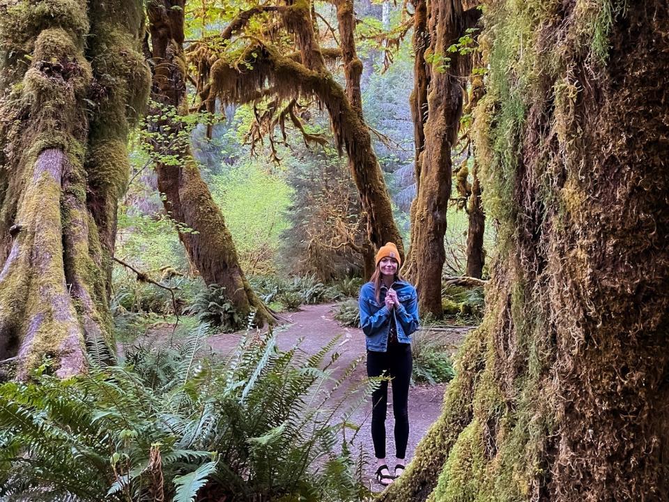 Emily stands between moss-covered trees in Olympic National Park.