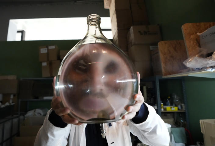 A worker holds a glass container with brandy, inside the distillery in Belgrade, Serbia, Friday, Nov. 11, 2022. The U.N.'s culture and education organization is set later this month to review Serbia's bid to include "social practices and knowledge related to the preparation and use of the traditional plum spirit - sljivovica" on the list of world intangible cultural heritage. (AP Photo/Darko Vojinovic)