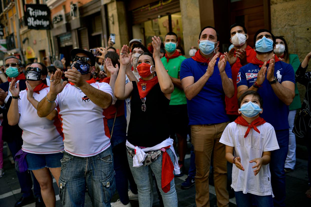 In this Saturday, June 20, 2020, photo, residents wear face masks, to protect against coronavirus, and San Fermin's red kerchief as people march the route of the running of the bulls while a singer performs a San Fermin's festival song in Pamplona, northern Spain. Spain reopened its borders to European tourists on Sunday, June 21, 2020, in a bid to kickstart its economy while Brazil and South Africa struggled with rising coronavirus infections.