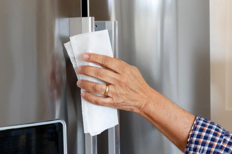 Man wipes down chrome refrigerator with cloth. 