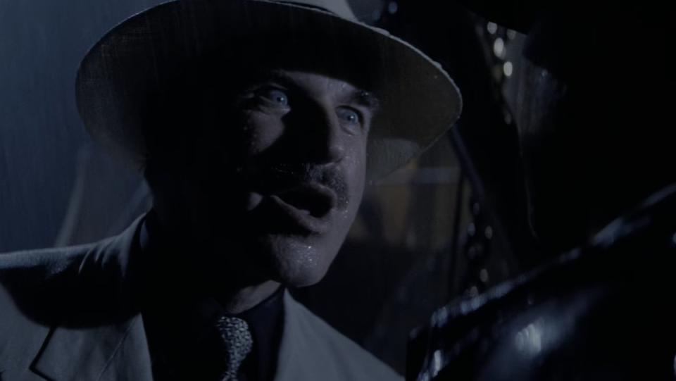 A mustachioed man in a Panama hat talks to Indiana Jones