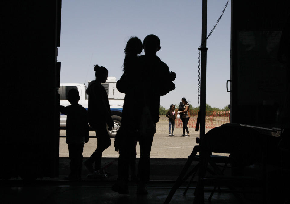 FILE - In this Wednesday, May 22, 2019 file photo migrants mainly from Central America guide their children through the entrance of a World War II-era bomber hanger in Deming, N.M. U.S. authorities are fast-tracking families' cases through the immigration courts in a pilot program aimed at discouraging many from making the journey to seek refuge in the United States. (AP Photo/Cedar Attanasio, File)
