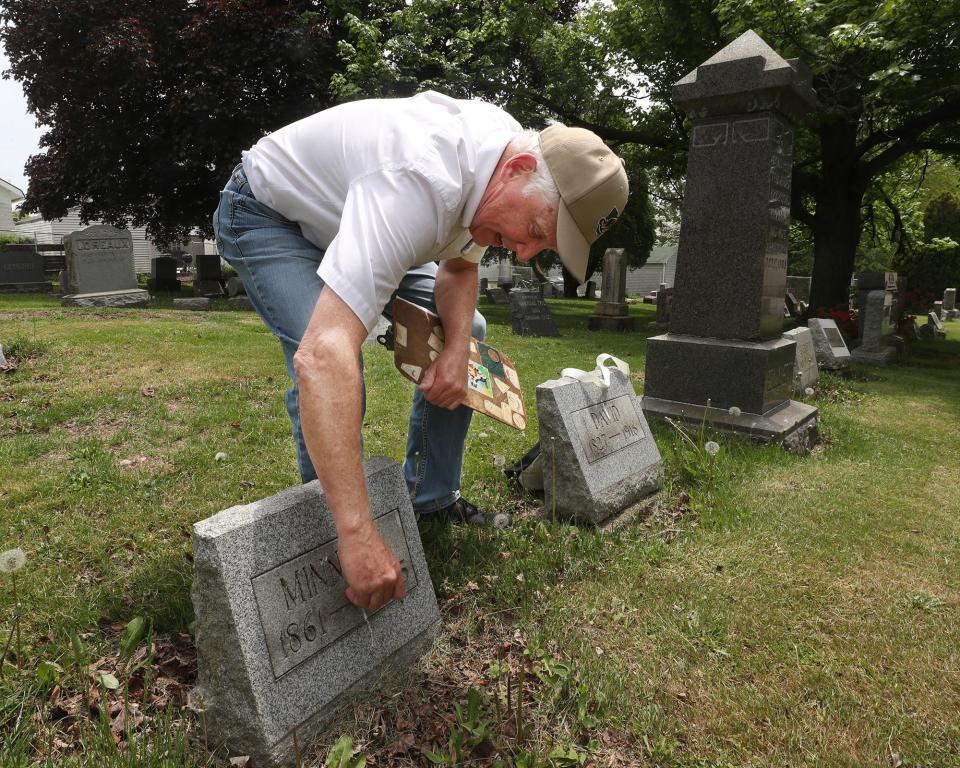 Jim Weyrick wipes off the headstone of Minnie Ellet who is buried next to her father David Ellet in a family plot at Ellet Cemetery in Akron.