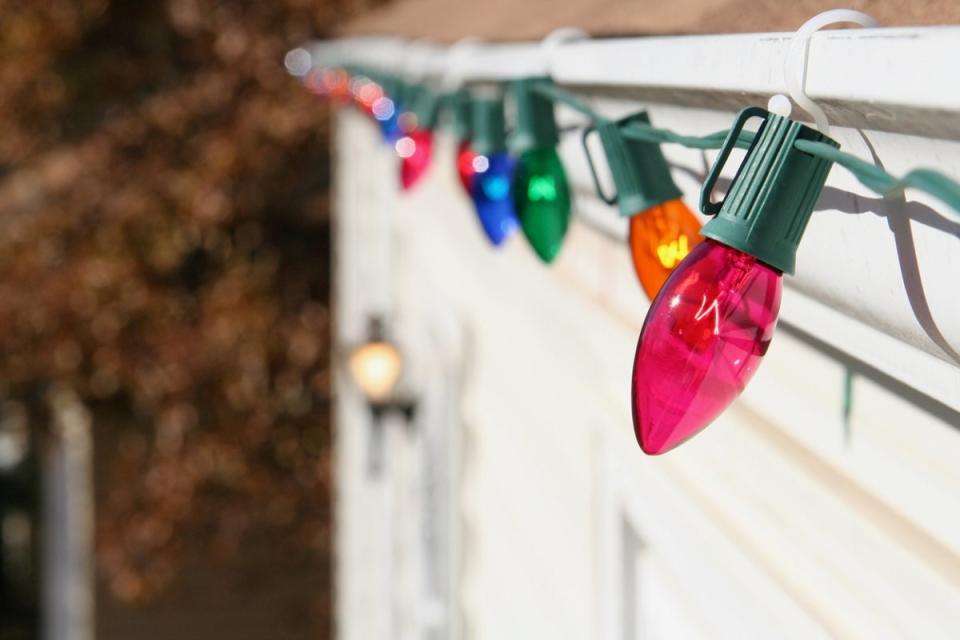 Large-bulbed Christmas lights hanging from plastic clips on a home's rain gutters.