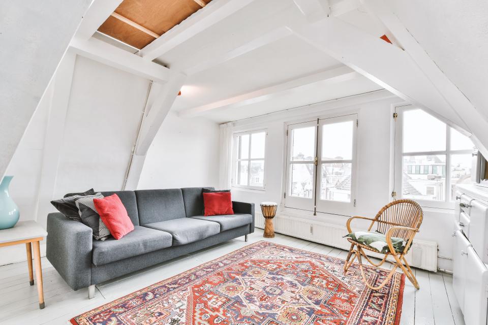 airy white living romo with gray couch, oriental rug, wicker chair and high ceilings