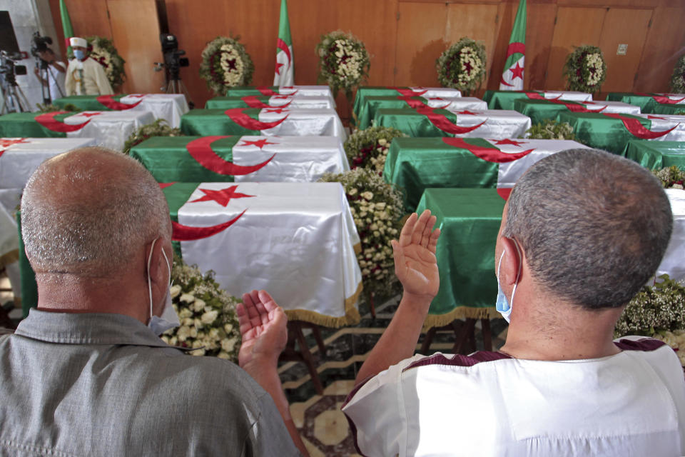 FILE - Men pray near the coffins of 24 Algerians at the Moufdi-Zakaria culture palace in Algiers, on July 3, 2020. After decades in a French museum, the skulls of 24 Algerians decapitated for resisting French colonial forces were formally repatriated to Algeria. French President Emmanuel Macron is heading to Algeria for a three-day official visit aimed at addressing two major challenges: boosting future economic relations while seeking at the same time a difficult reconciliation of memories, 60 years after the North African country won its independence from France. (AP Photo/Toufik Doudou, File)