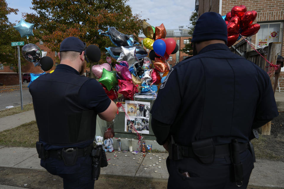 Members of Valentis Private Security pause at a makeshift memorial of balloons, stuffed animals, and photographs, Monday, Nov 6, 2023, in Cincinnati, for Dominic Davis, an 11-year-old boy, who was killed in a weekend shooting. Police Chief Terri Theetge told reporters Sunday that a shooter in a sedan fired 22 rounds "in quick succession" into a crowd of children just before 9:30 p.m. Friday on the city's West End. (AP Photo/Carolyn Kaster)