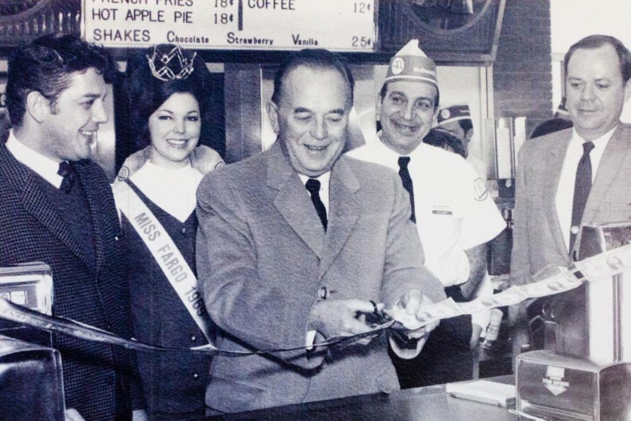 Ray Kroc cutting a ribbon of one dollar bills.