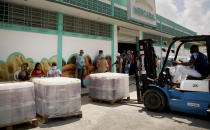 A worker moves goods with a forklift at the entrance of Mercabal wholesale market where customers wait to enter in Havana, Cuba, Thursday, July 30, 2020. The government is letting private businesses buy wholesale for the first time. (AP Photo/Ismael Francisco)