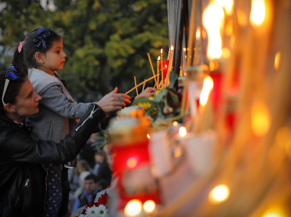 A child lights candles next to a portrait of slain television reporter Viktoria Marinova during a vigil at the Liberty Monument in Ruse, Bulgaria, Monday, Oct. 8, 2018. Bulgarian police are investigating the rape, beating and slaying of a female television reporter whose body was dumped near the Danube River after she reported on the possible misuse of European Union funds in Bulgaria. (AP Photo/Vadim Ghirda)