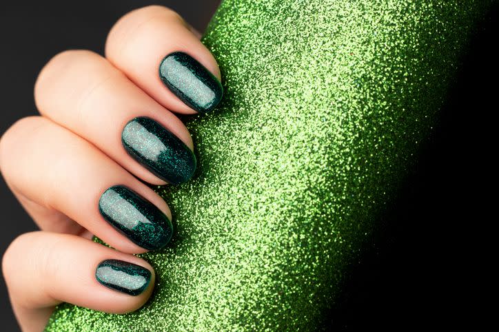 female hand with beautiful holiday manicure green glittered nails with glitter paper background