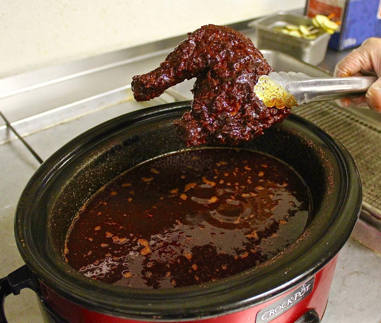 Bishop's Meat & 3 dips a chicken leg quarter into a spicy sauce for hot chicken.